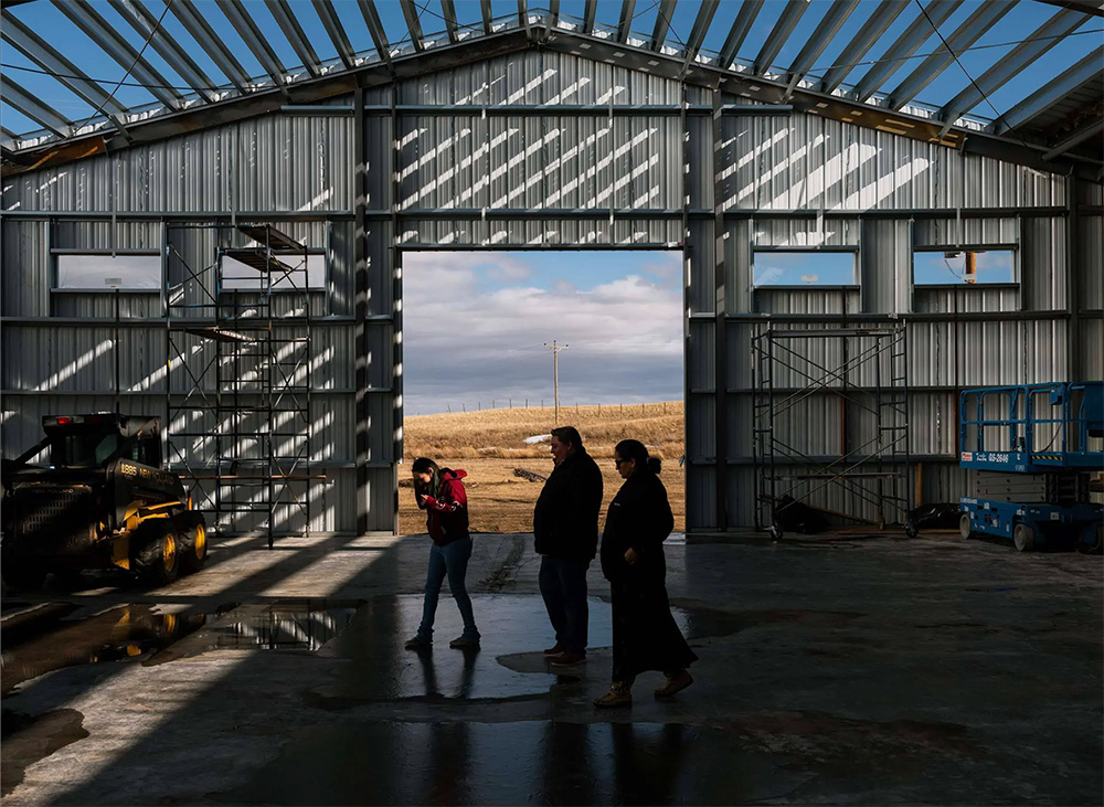 Blackfeet Community College President Brad Hall (center) and Institutional Development Director Melissa Weatherwax (right) walk through a half-finished building meant to host a college program training workers for the tribe’s slaughterhouse. Without federal grants, the Montana college might pause the building project. Credit:Rebecca Stumpf for ProPublica